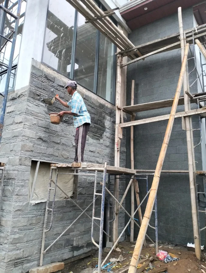 Proses pembersihan permukaan dinding batu pada area luar rumah dengan cara yang hati-hati.