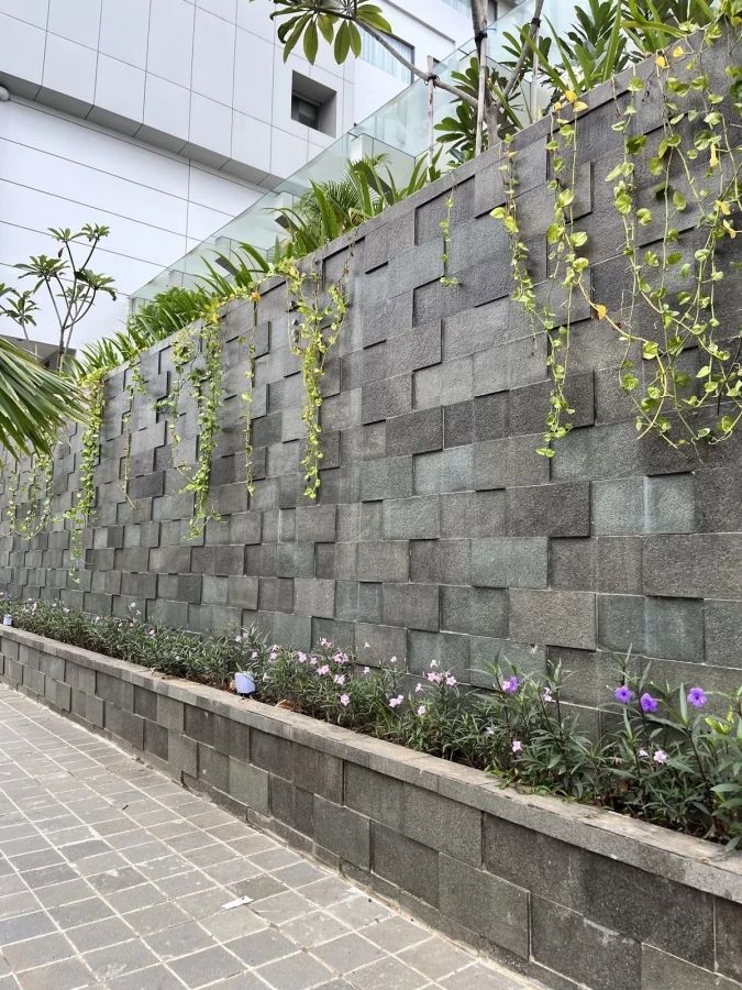 Dinding taman outdoor menggunakan batu andesit warna abu gelap dengan pola susun bata timbul di area walkway.