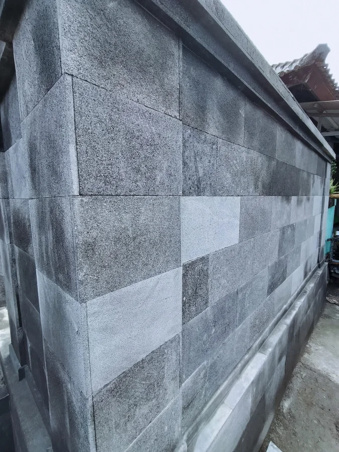 Dinding pagar luar yang dilapisi batu alam candi bertekstur pori dengan pola susun bata, menampilkan warna abu-abu alami kondisi batu sebelum proses vernish.