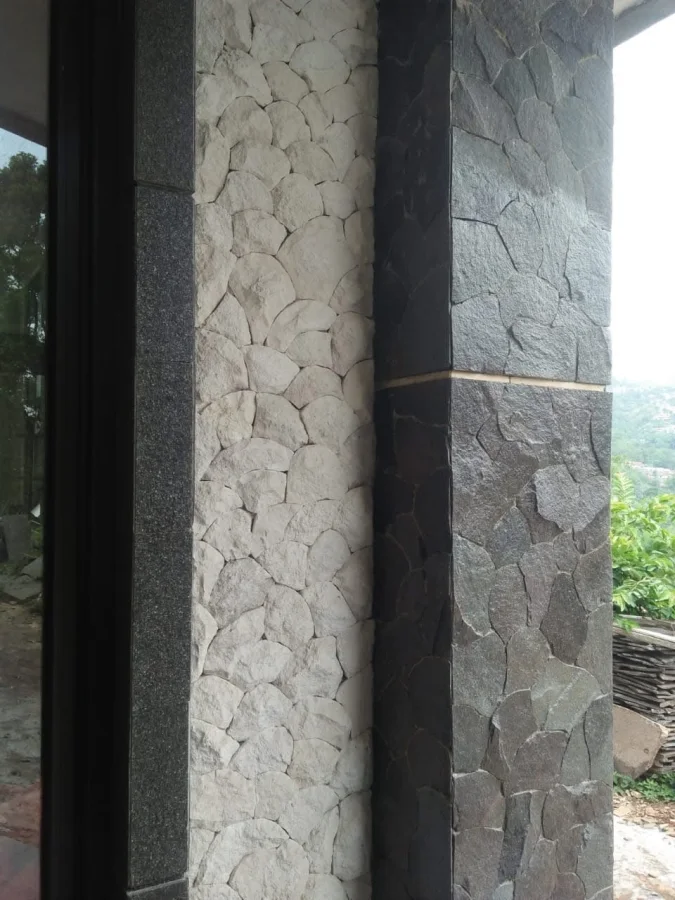 Fasad bangunan dengan pilar batu templek purwakarta acak, dinding batu limestone putih, dan tepian andesit bakar hitam presisi.